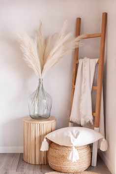 a vase with some white feathers in it next to a wooden chair and towel rack