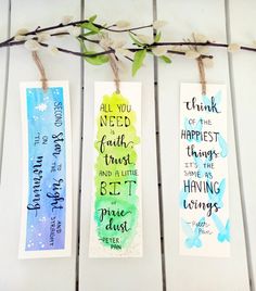 three watercolor bookmarks with bible verses on them hanging from a twig