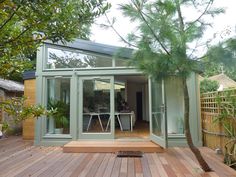 a wooden deck with a table and chairs on it next to a tree in front of a house