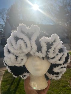 a person holding up a white hat with flowers on it in front of the sun