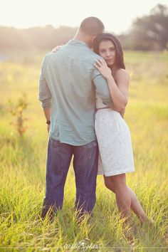 a man and woman are standing in the grass with their arms wrapped around each other