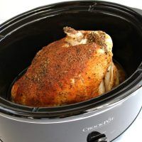 a close up of a cooked chicken in a crock pot on a white table