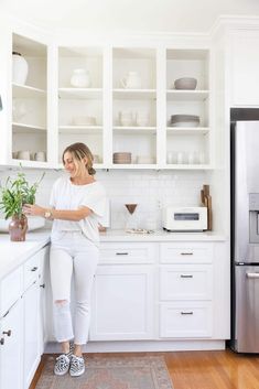 a woman standing in a kitchen next to a refrigerator and counter top with dishes on it