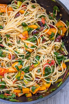 a pan filled with pasta and vegetables on top of a wooden table