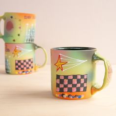 two colorful coffee mugs sitting on top of a wooden table next to each other