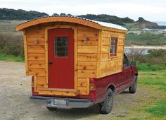 a red pickup truck parked in front of a small wooden cabin on the side of a road