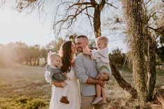 a man, woman and two children are standing in front of a tree while the sun shines on them