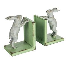 two small figurines of rabbits playing with each other on green stands, one holding the door open