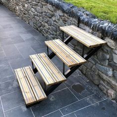 two picnic tables sitting next to each other on top of a stone walkway near a rock wall