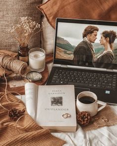 an open laptop computer sitting on top of a bed next to a cup of coffee