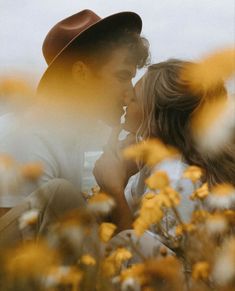 a man in a hat kissing a woman on the cheek with yellow flowers around him