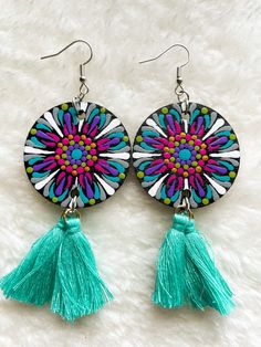 a pair of colorful earrings with tassels on top of white furnishing