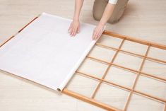 a person kneeling on the floor next to a sheet of paper that has been cut into squares