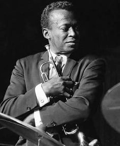 a black and white photo of a man in a suit with his arms crossed holding a trumpet