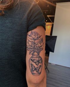 a woman with a tattoo on her arm holding a vase filled with flowers and butterflies