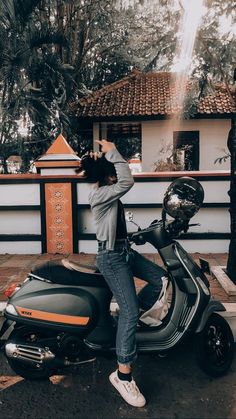 a person standing next to a scooter in front of a building and trees