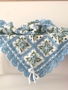 a crocheted blue and white blanket with flowers on it, hanging from a hook