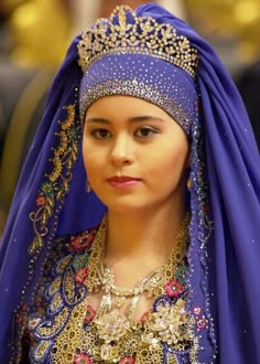 a woman wearing a blue veil and headdress with jewels on her head is looking at the camera