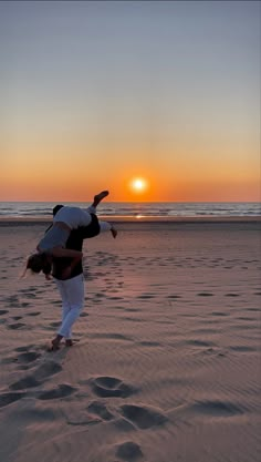 a person doing a handstand on the beach at sunset