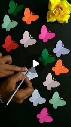 someone cutting out paper butterflies with scissors and a yellow flower in the background on a black surface