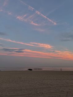 the sky is pink and blue as it sets on an empty beach with boats in the distance