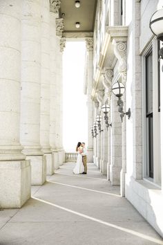 a bride and groom standing on the sidewalk in front of an old building with columns