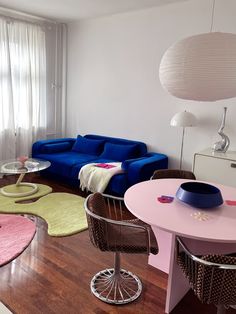 a living room filled with furniture and a blue couch next to a pink table on top of a hard wood floor