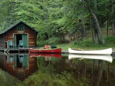 a red boat sitting next to a wooden cabin on top of a lake in the woods