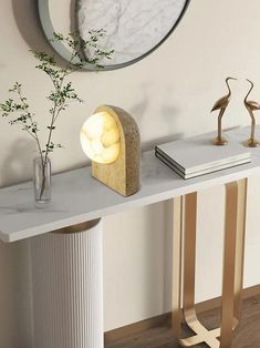 a white table with a vase and some books on it next to a round mirror