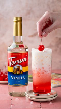 a person is holding a cherry in front of a bottle of torani vanilla rum