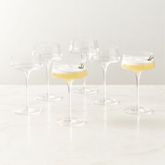 five glasses filled with yellow liquid and topped with an orange garnish sit on a marble surface