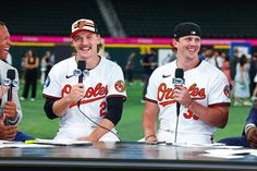 three baseball players sitting at a table with microphones in front of them and people standing around