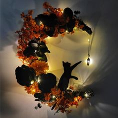 a wreath made out of pumpkins and lights with a cat on it's back