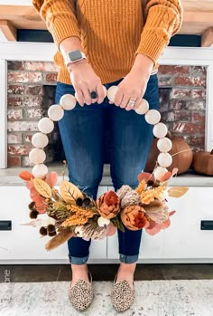 a woman standing in front of a fireplace holding onto a wreath made out of fake flowers