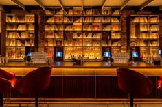 a bar with red chairs and bookshelves in front of it at night time