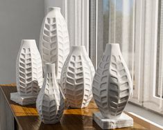 three white vases sitting on top of a wooden table next to a windowsill