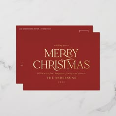 a merry christmas card with gold lettering on a red envelope sitting on a marble surface