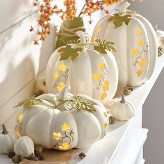 white pumpkins decorated with yellow flowers and leaves are sitting on a shelf in front of a window