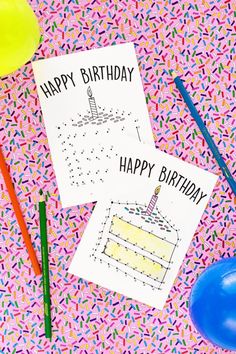 two birthday cards sitting on top of a table next to balloons and confetti