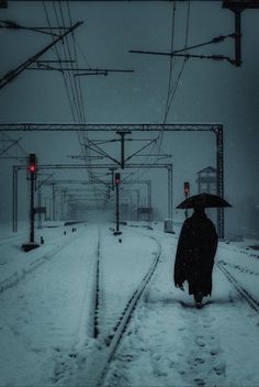 a person with an umbrella is walking down the train tracks in the snow at night