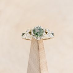 a green and white diamond ring sitting on top of a wooden stand in front of a beige background