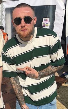 a man with tattoos standing in front of a sign