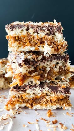 three pieces of chocolate and coconut bars stacked on top of each other with nuts scattered around them