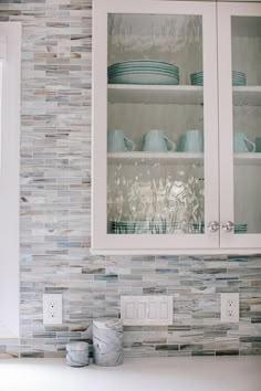 a kitchen with white cabinets and blue dishes on the counter top in front of glass fronted cupboards