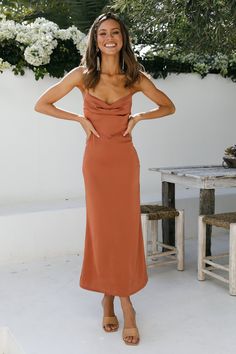 a woman standing in front of a table wearing an orange dress and smiling at the camera