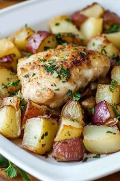 chicken, potatoes and parsley in a white dish on a wooden table with green garnish