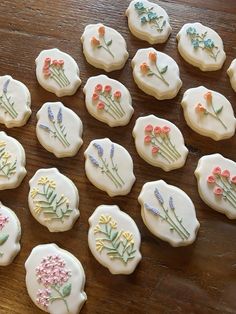 twelve decorated cookies with flowers on them sitting on a wooden counter top, ready to be eaten