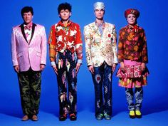 three men in colorful suits and tuxedos standing next to each other on a blue background