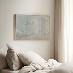 an unmade bed with white sheets and pillows in front of a painting on the wall