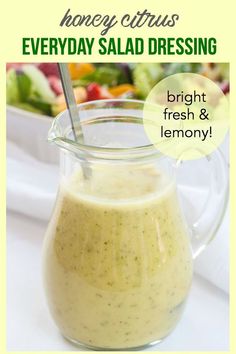 a glass pitcher filled with dressing next to a bowl of salad